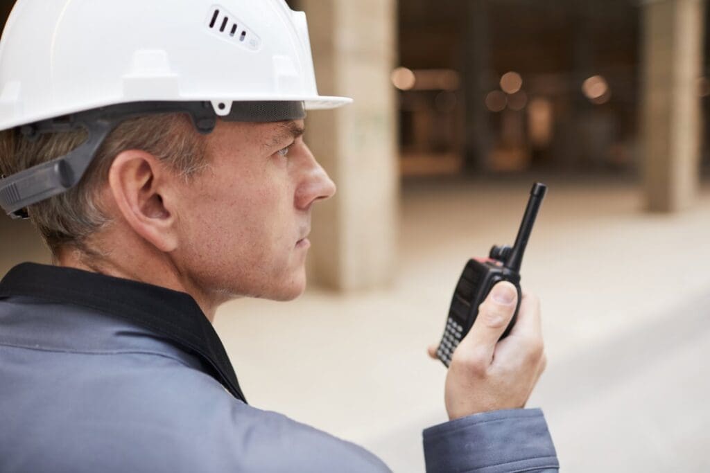 Sicherheitsdienst in Berlin sichert eine Baustelle mit Funkgerät und Helm.